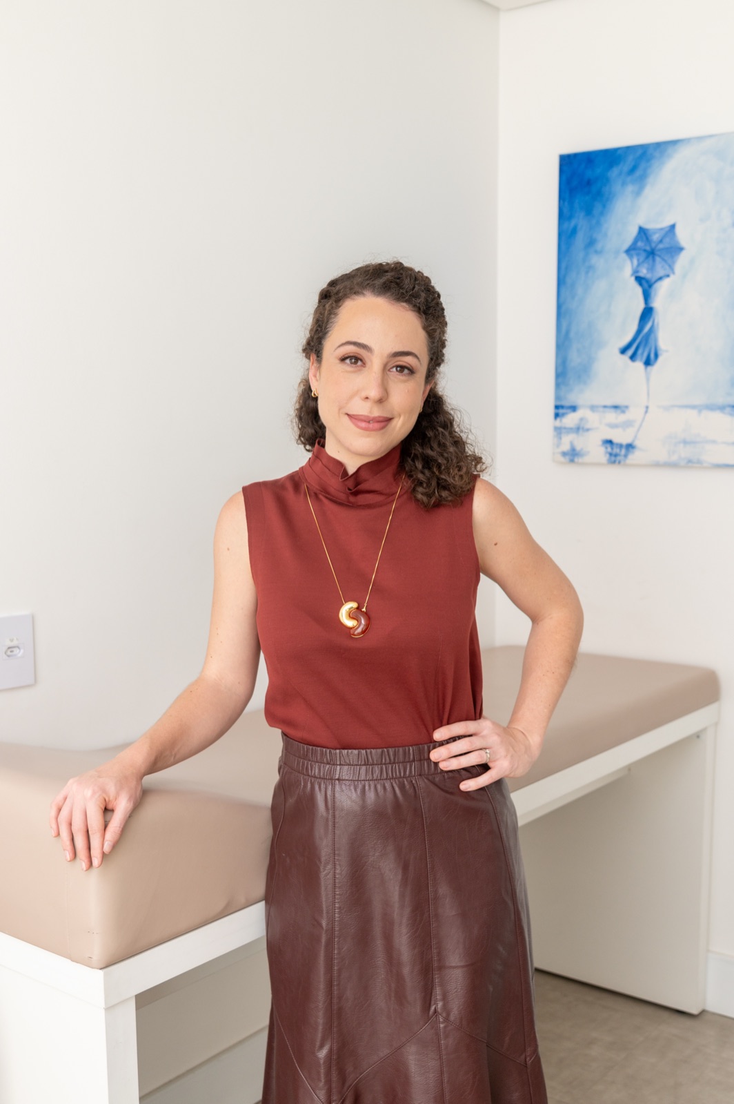 Foto da Dra. Julia Melardi apoiada na maca de atendimento do consultório
